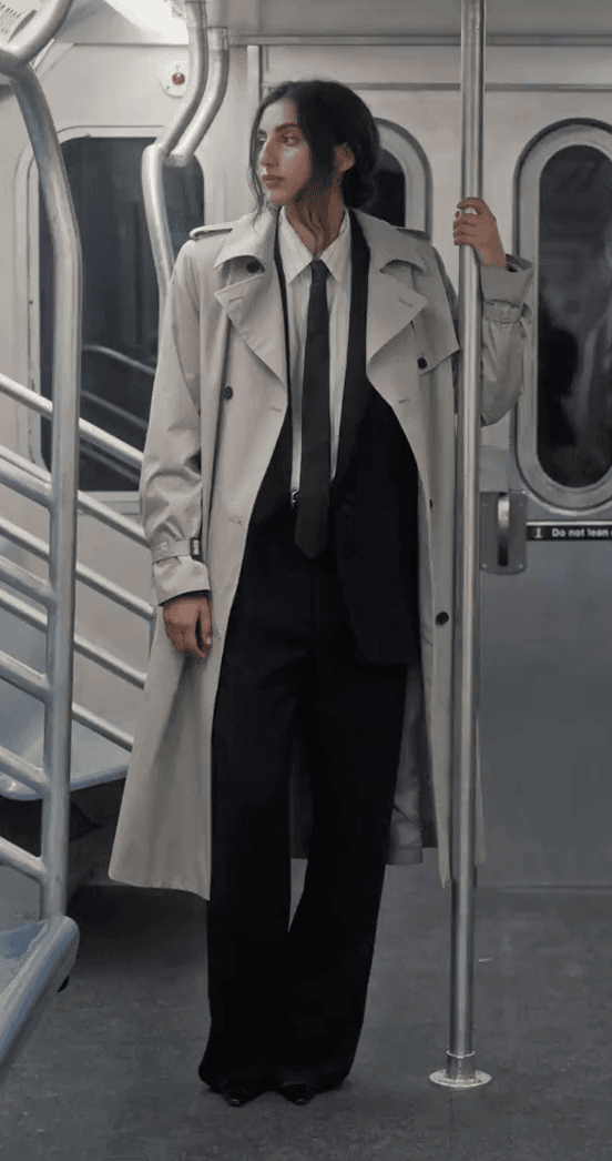 A model in a cream trench coat and black suit holding a subway pole