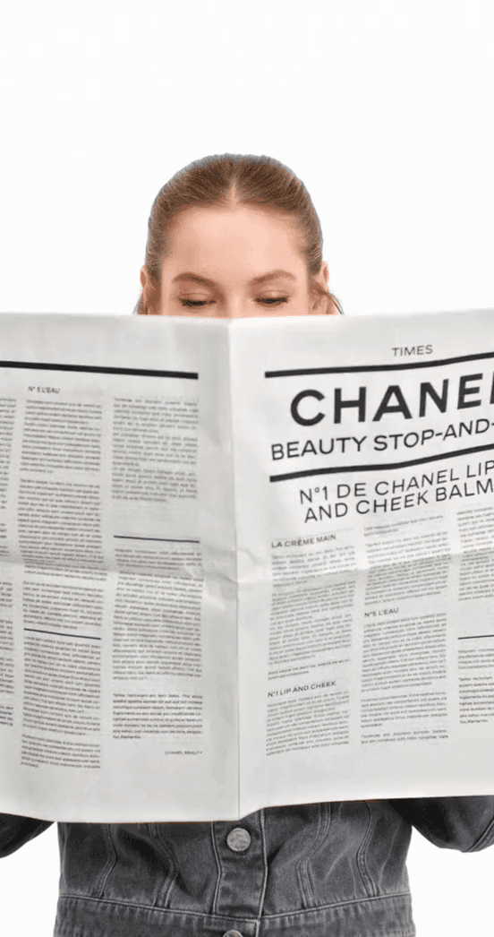 A person holding a newspaper with a Chanel Beauty Stop-and-Shop headline