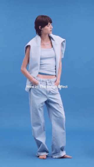 Aritzia: a model in a pale blue knit set and jeans on a blue backdrop