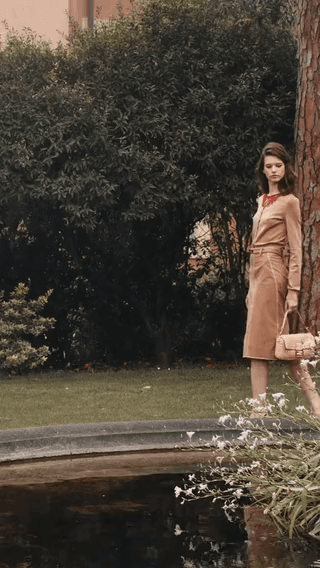 Chanel: a model in a camel cardigan and skirt by a garden pond