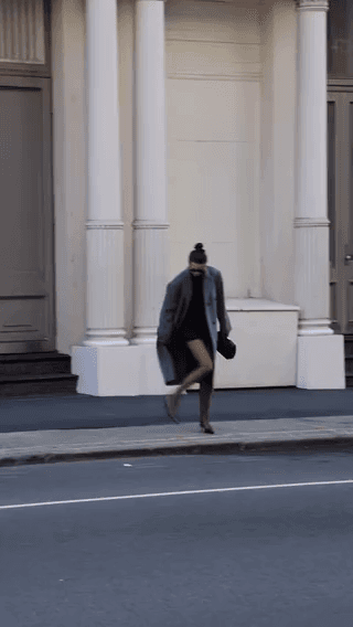 Oak + Fort: a woman in a grey coat walking past a colonnade