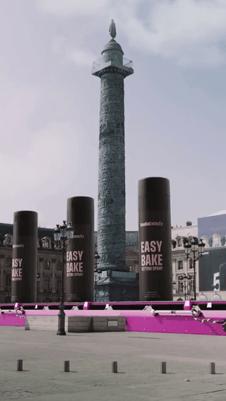 Huda Beauty: giant Easy Bake setting-spray cans beside a city column